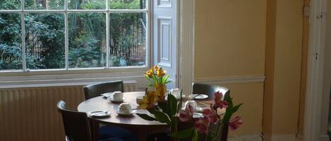 A dining table set with tea cups, saucers, and a vase of flowers.