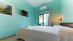 A room with teal walls, a bed with white linens, a mounted TV, and a window with curtains. - Hostal Sahaba Zahora (Barbate)