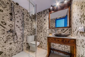 Une salle de bain avec des carreaux décorés, une douche en verre, des toilettes blanches et un meuble-lavabo en bois avec un évier.