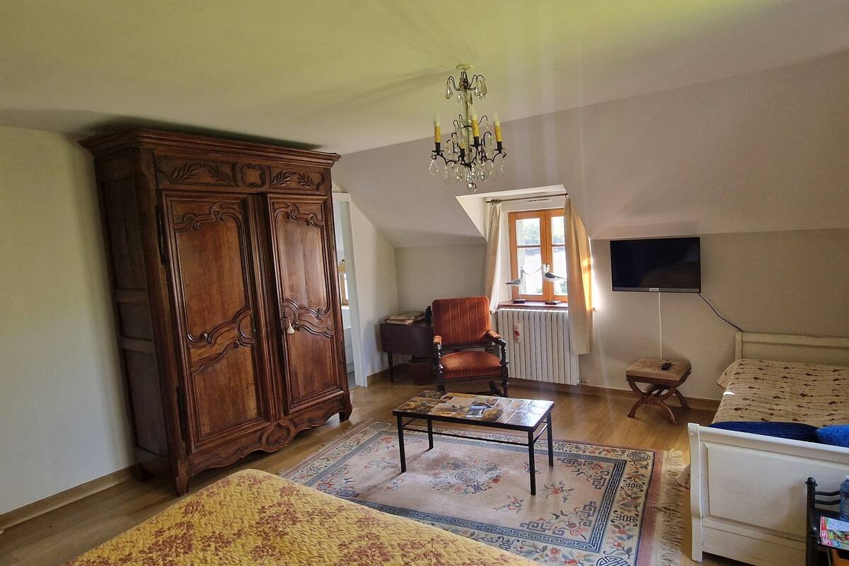 A spacious living room with a large wooden cabinet, a sofa, a coffee table, and a television mounted on the wall.