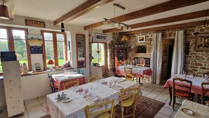 Un coin repas rustique avec des murs en pierre, des poutres en bois et plusieurs tables dressées pour le dîner.