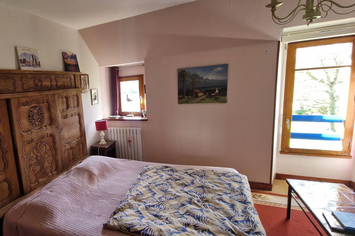 A bedroom with a bed, a wooden headboard, a red lamp, and a window with a view.