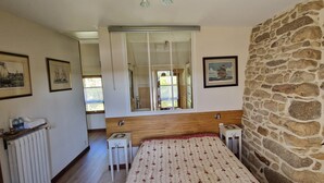 Une chambre à coucher avec une tête de lit en bois, un lit recouvert d’une couvre-lit à motifs floraux, un mur en pierre et une fenêtre donnant sur l’extérieur.