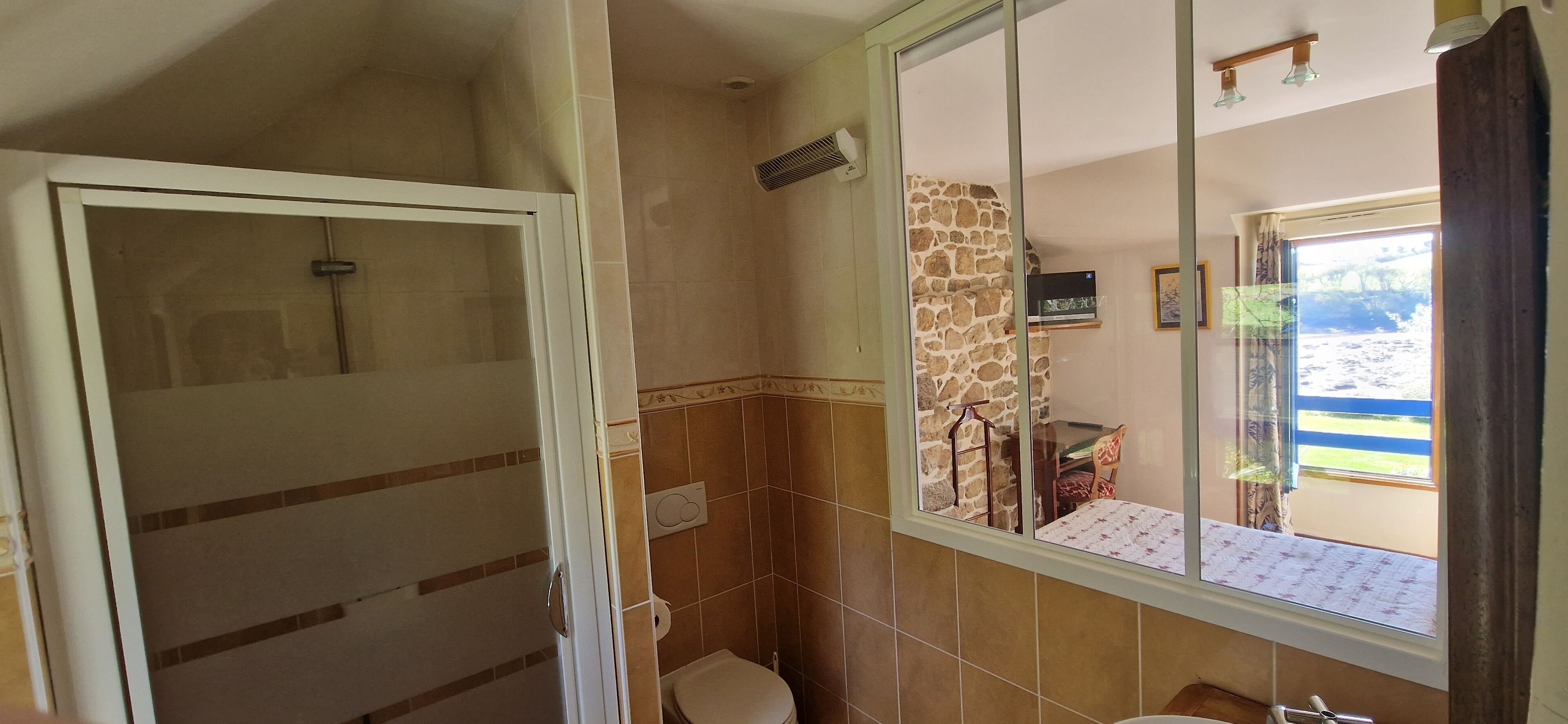 A bathroom with a shower, toilet, and a window with a view of the outdoors.