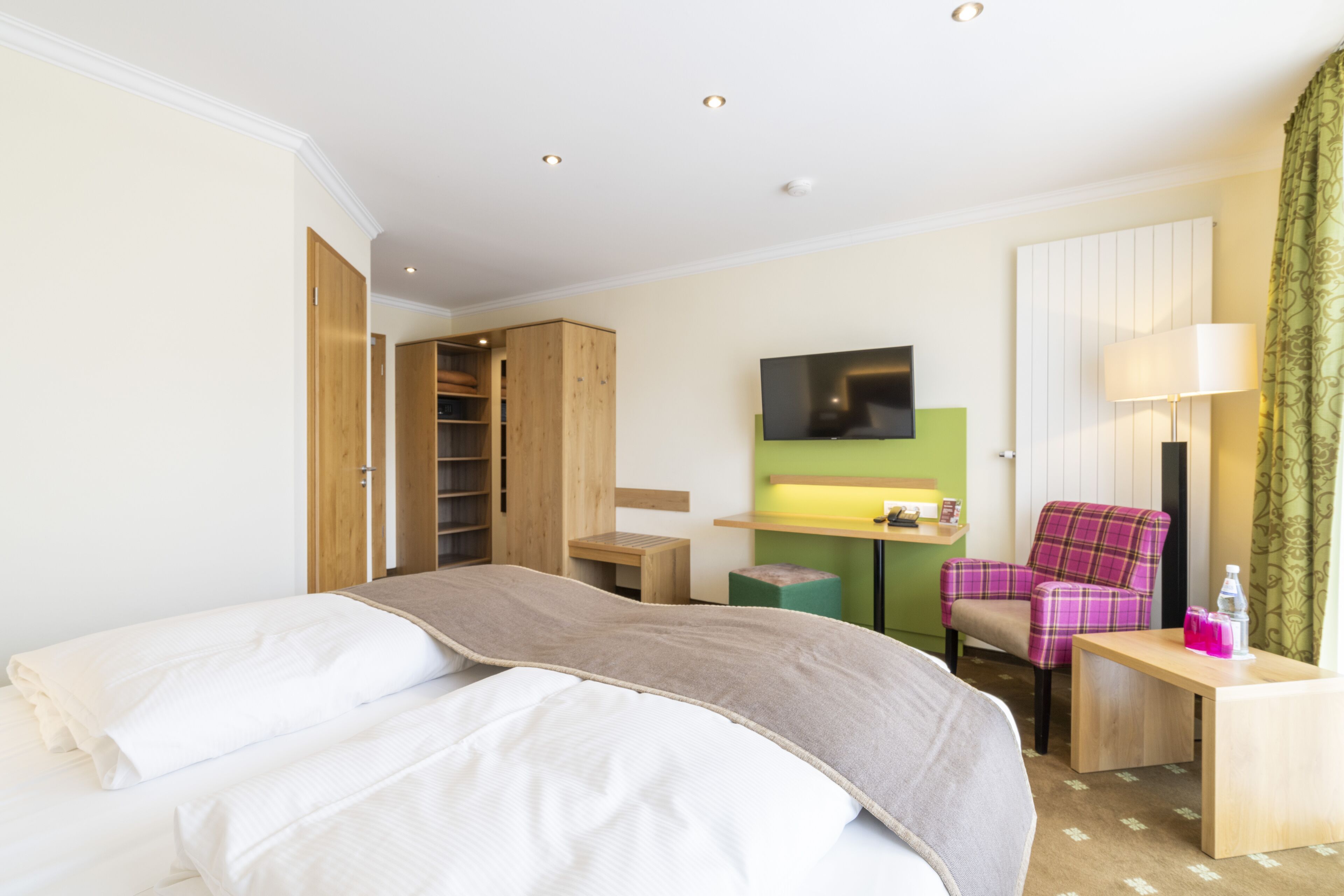 A hotel room with a bed, a desk, a chair, a TV, and a wardrobe.