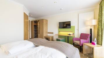 A hotel room with a bed, a desk, a chair, a TV, and a wardrobe.