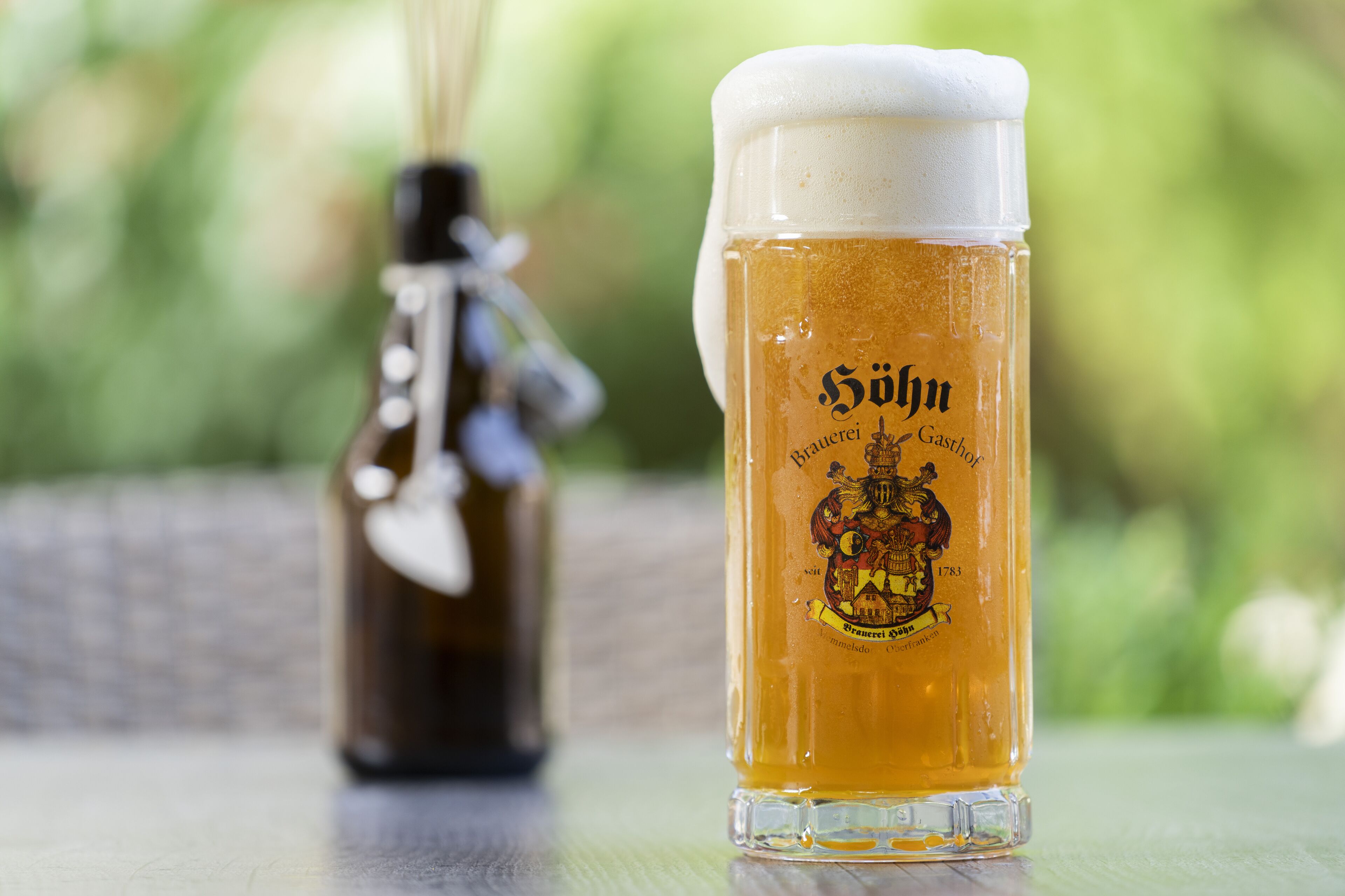 A glass of beer with a logo and a bottle in the background.