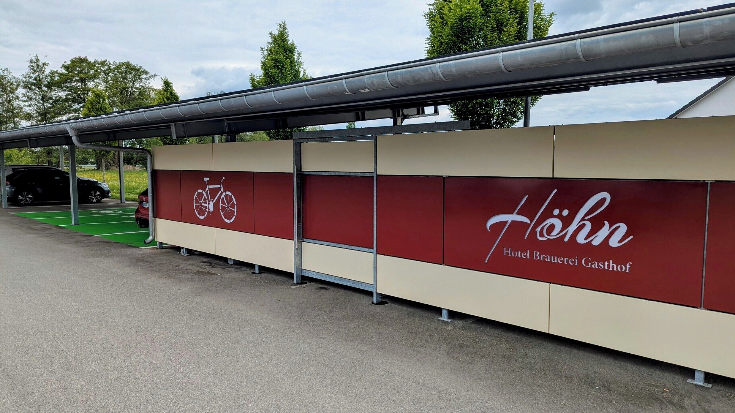 A building with a sign for Hotel Brauerei Gasthof Höhn, featuring a bicycle symbol and a green parking area.