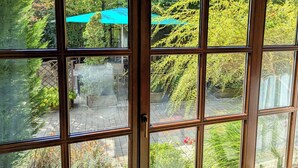A view through a window with a wooden frame, revealing an outdoor area with a paved walkway, a blue umbrella, and greenery. - Hotel Brauerei Gasthof Höhn (Memmelsdorf)