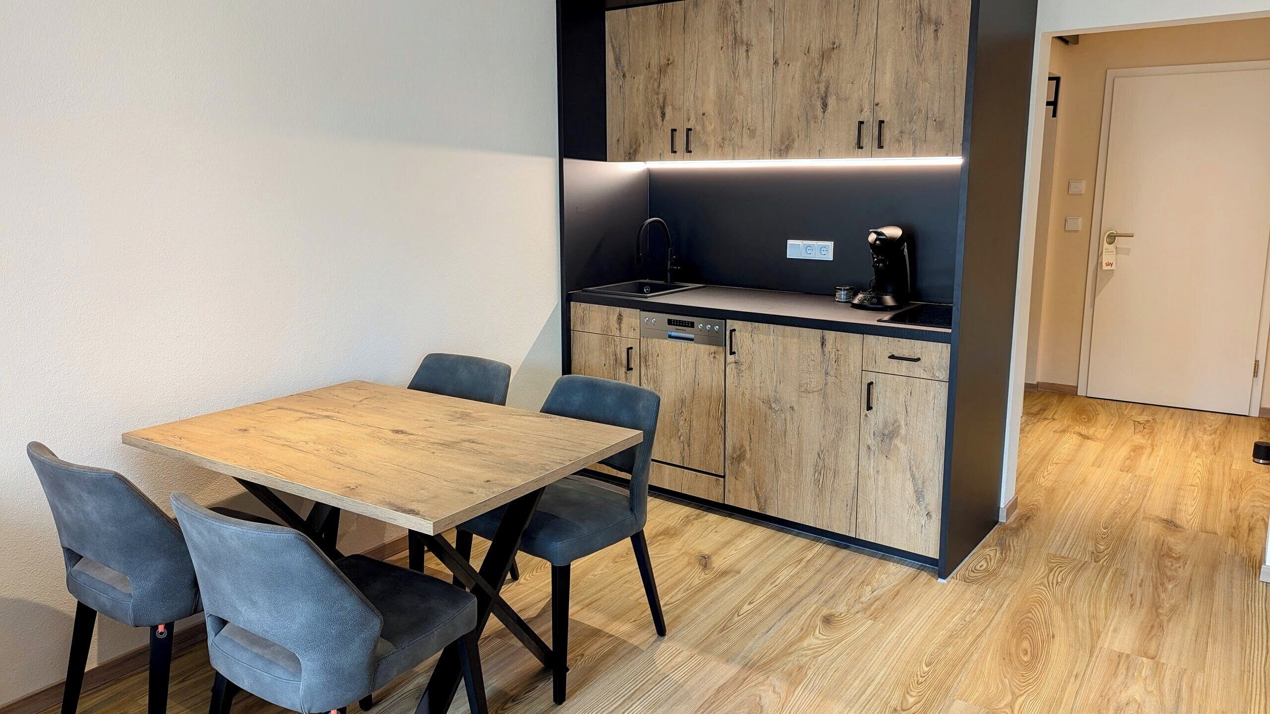 A compact kitchen with a wooden table and chairs, a built-in oven, and a coffee machine.