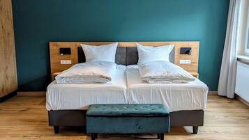 A double bed with white linens, a wooden headboard, and a matching bench.