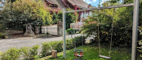 Un jardín con un columpio, una estructura de piedra y una casa con techo inclinado.