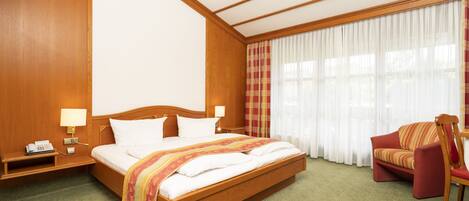 A hotel room with a large bed, a chair, a nightstand, and a window with curtains.