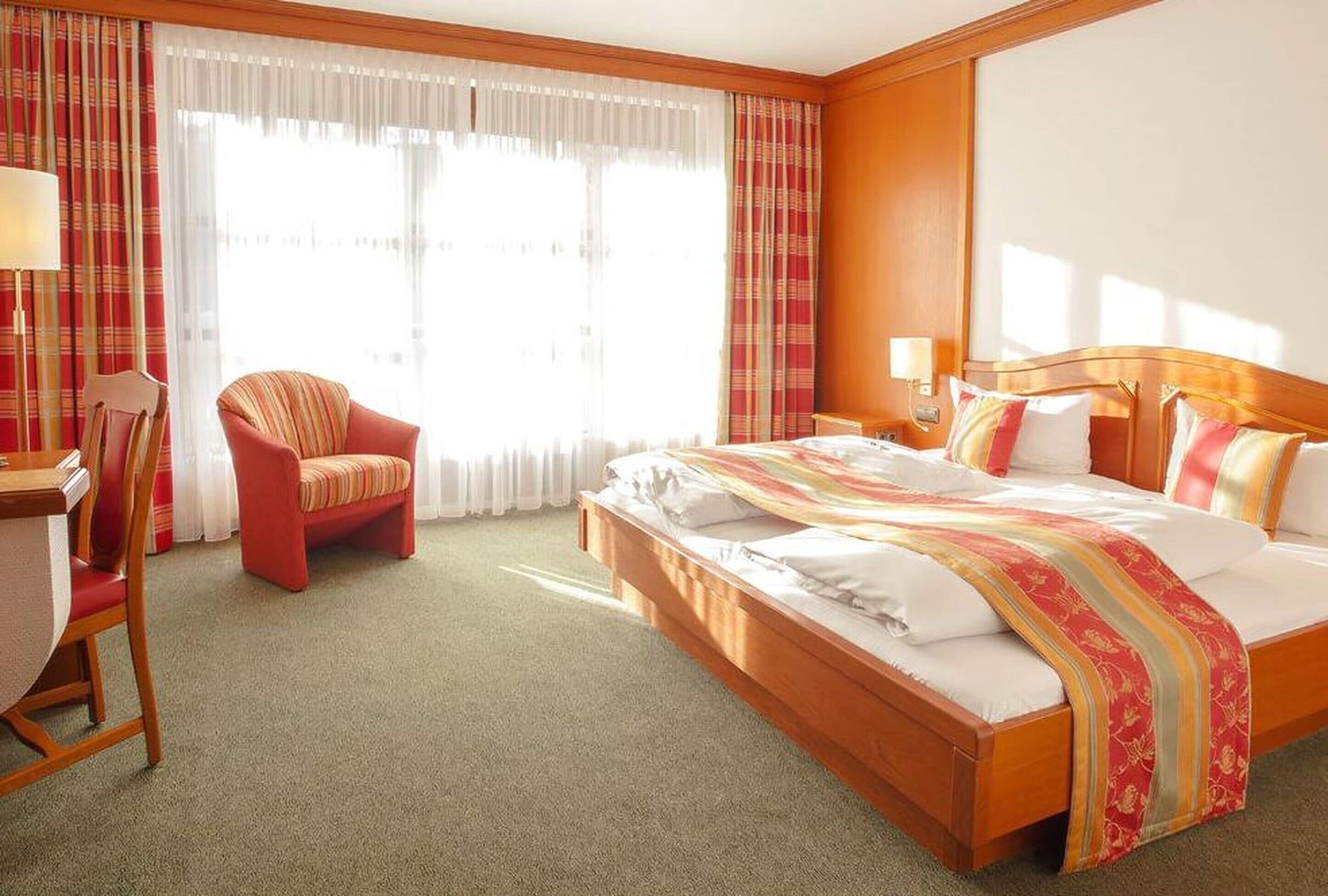 Una habitación de hotel con una cama grande, una silla, un escritorio y una ventana con cortinas.