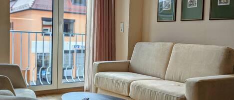 A living room with a sofa, a small table, and a balcony with a railing.