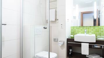 A modern bathroom with a glass shower enclosure, a white toilet, a sink with a green backsplash, and a mirror above the sink.