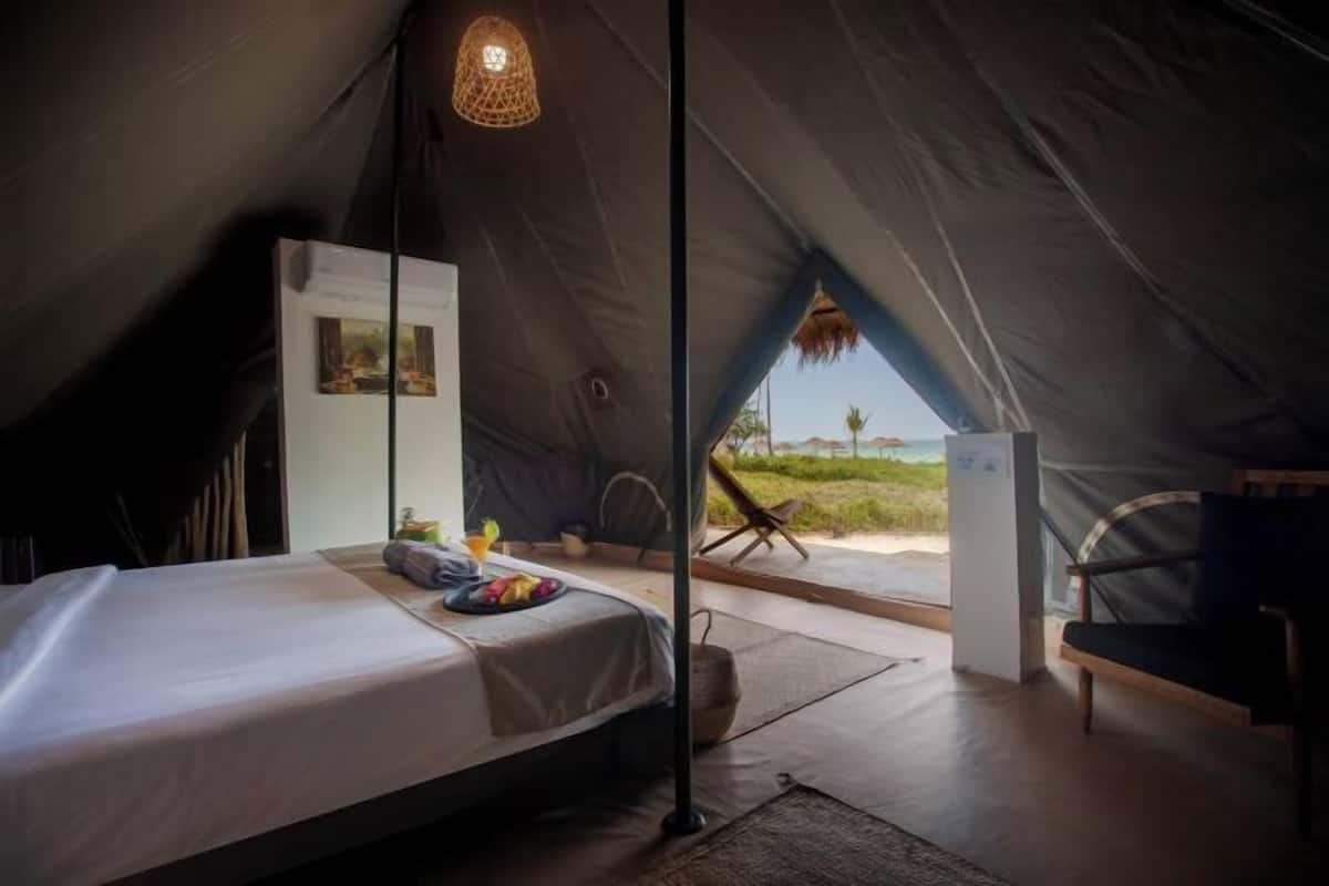 A tent with a bed, a hanging light fixture, a chair, and a view of the landscape.