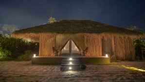 A thatched-roof structure with a central entrance and steps leading up to it, surrounded by natural vegetation. - Tamu Koh Rong (Koh Rong)