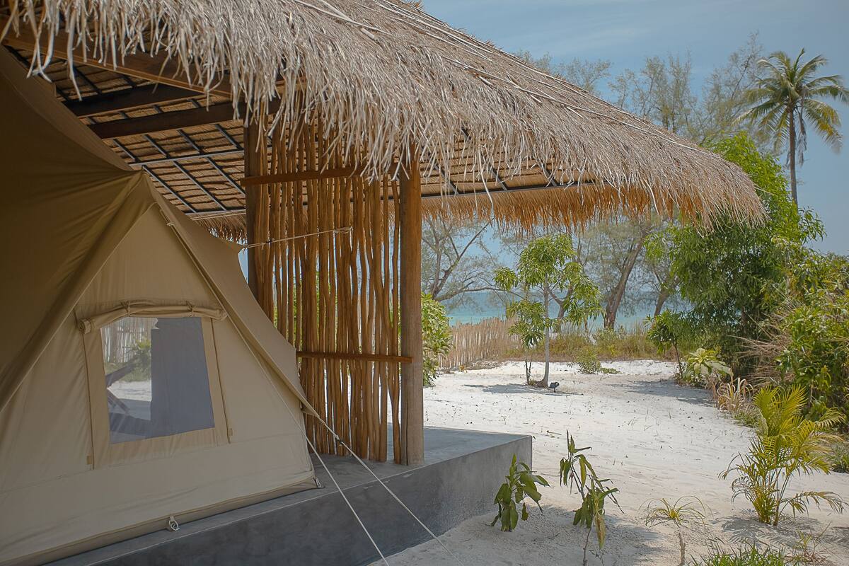 A beachside tent with a thatched roof, surrounded by sand and sparse vegetation.