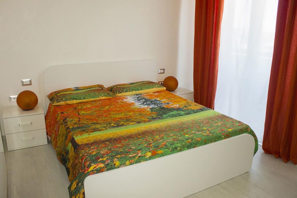 Une chambre à coucher avec un lit, des tables de chevet blanches et une fenêtre avec des rideaux.