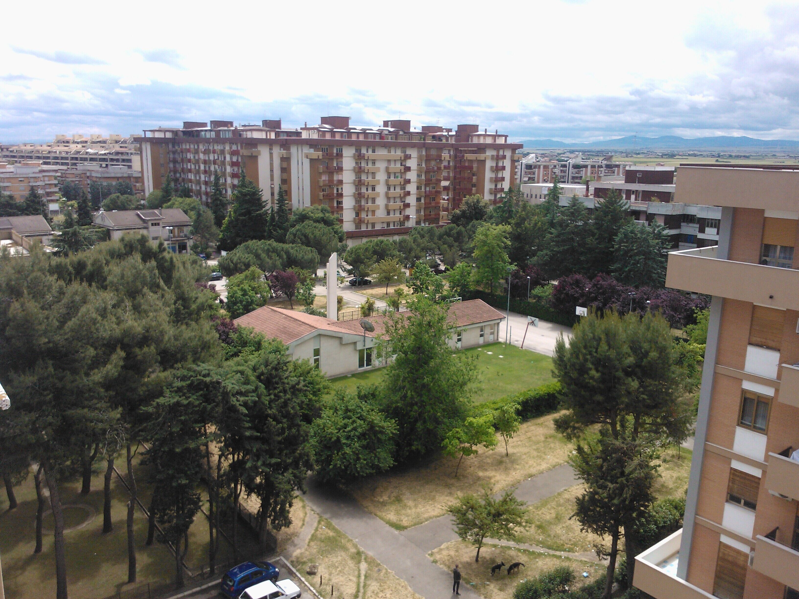 A residential area with apartment buildings, a small park with trees, and a clear sky.