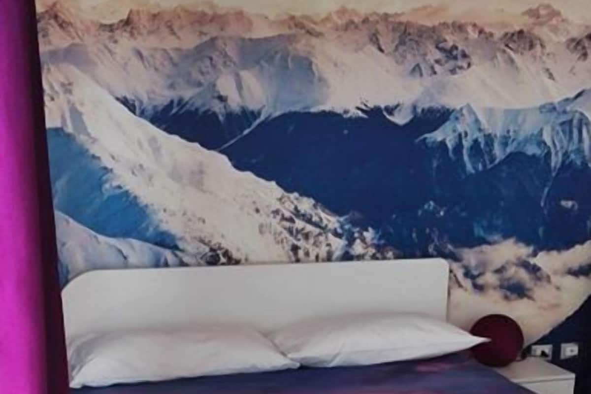 Un lit avec une fresque représentant un paysage de montagne peinte sur le mur qui se trouve derrière.
