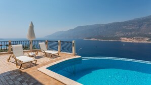 Ein Poolbereich mit Liegestühlen und Sonnenschirm, mit Blick auf eine Küstenlandschaft.