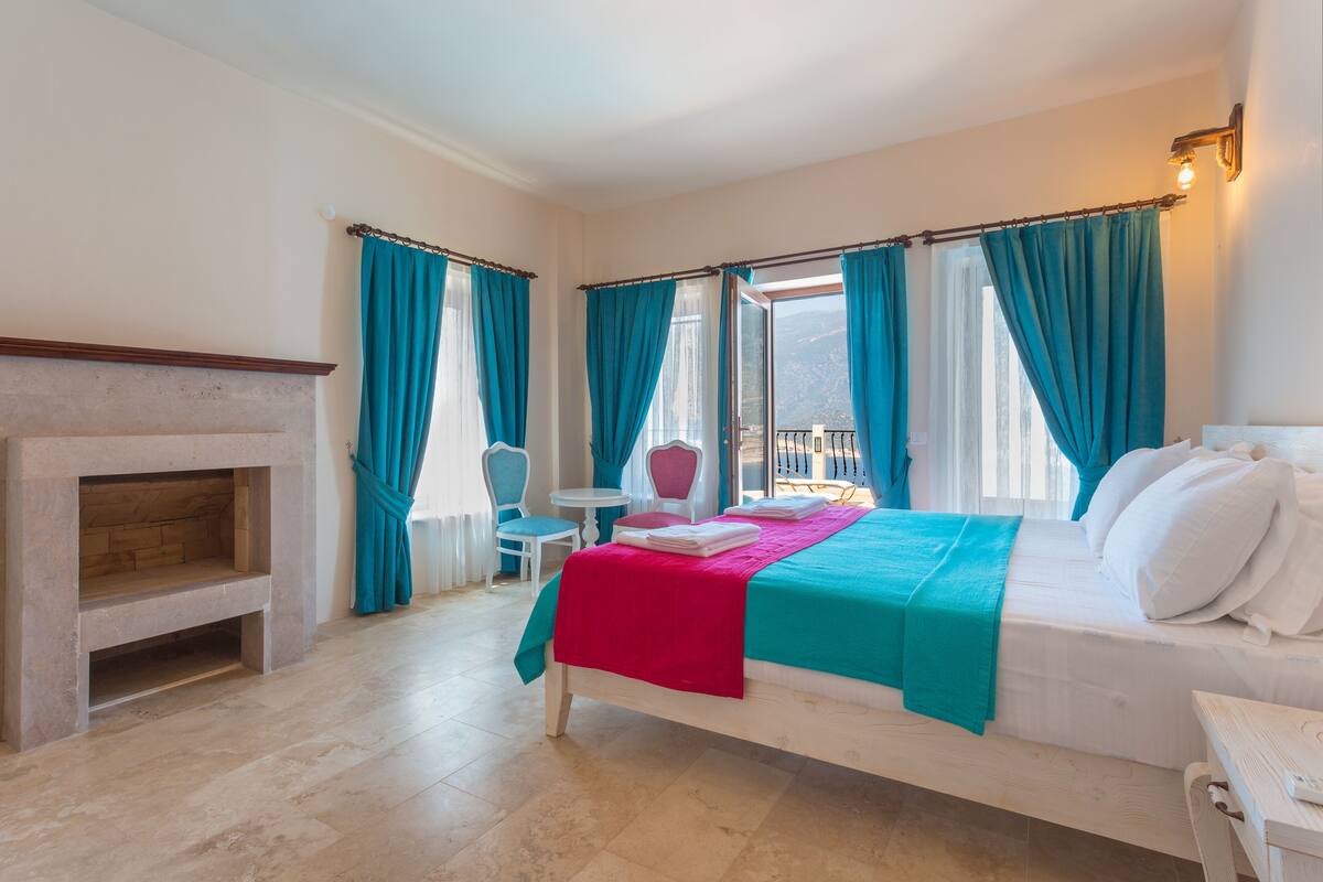 Een slaapkamer met een bed, een open haard, een balkon en uitzicht op de omgeving.