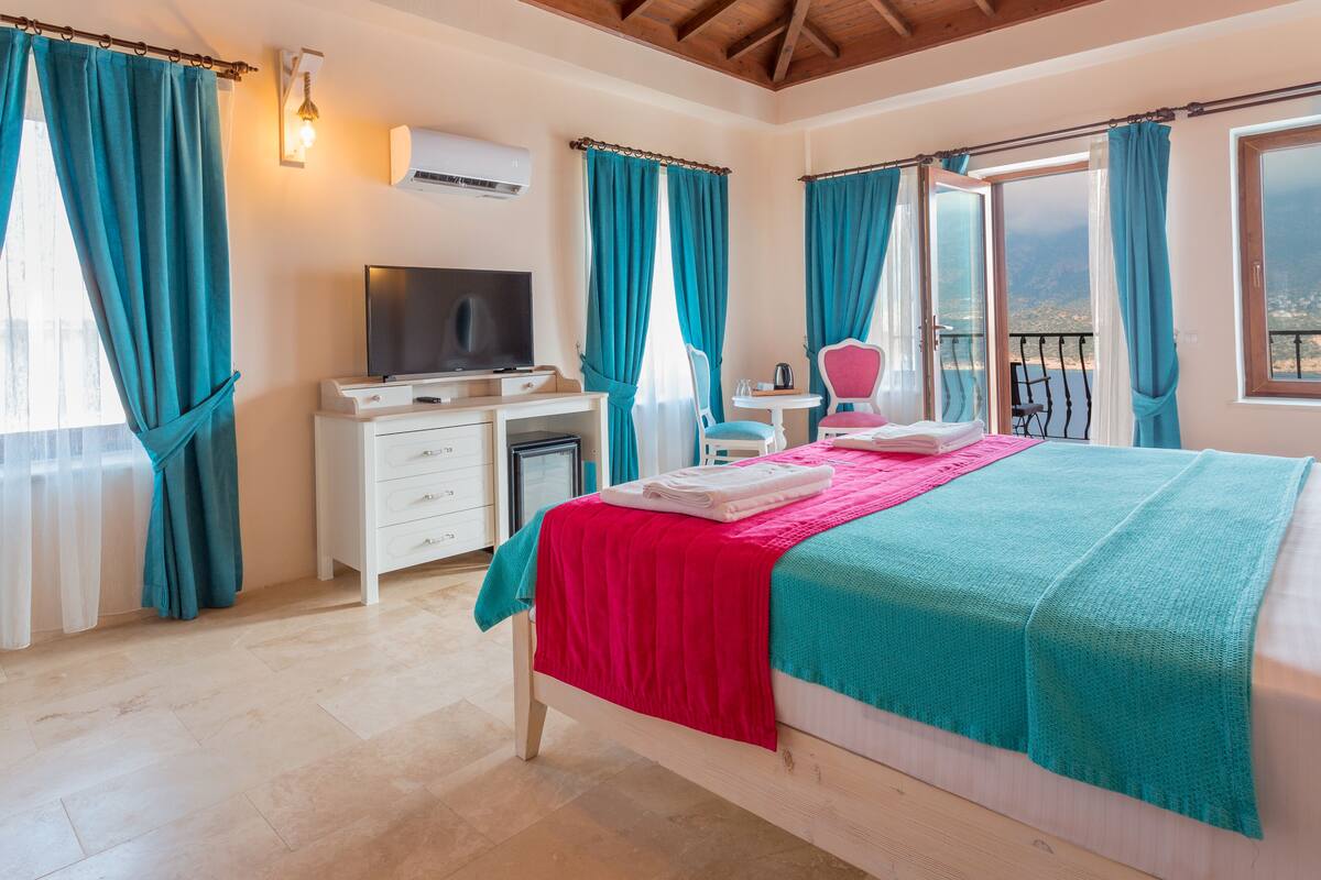 Een slaapkamer met een bed, een bureau, een televisie en een balkon met uitzicht.