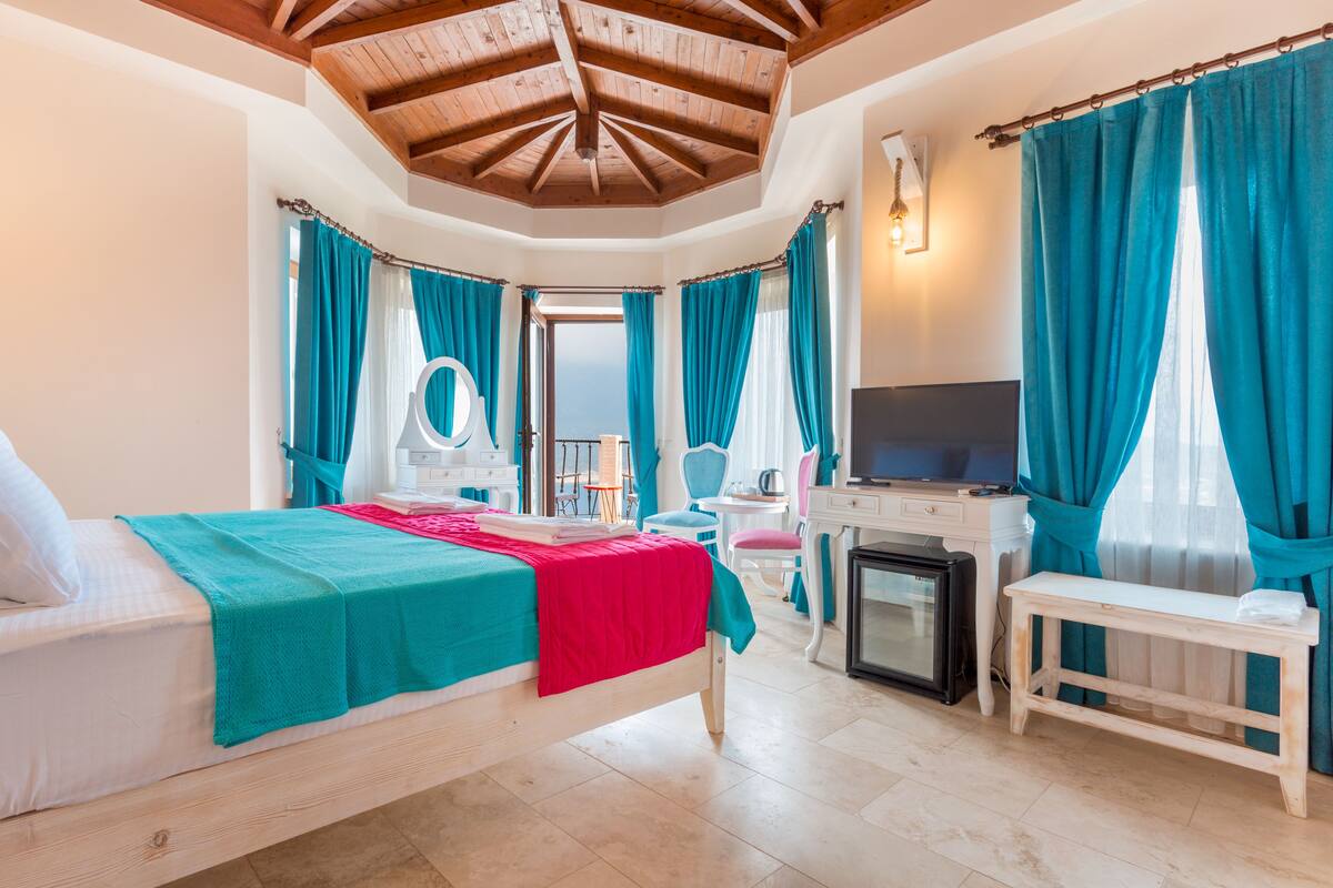 Een slaapkamer met een bed, een bureau, een televisie en uitzicht op zee.