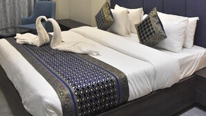Hotellihuone, jossa on suuri sänky, kattotuuletin, seinään kiinnitetty valaisin ja sininen tuoli.