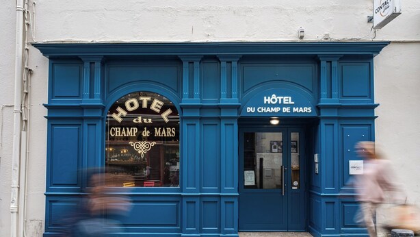 Fachada azul de um hotel com o nome 'Hôtel du Champ de Mars' visível.