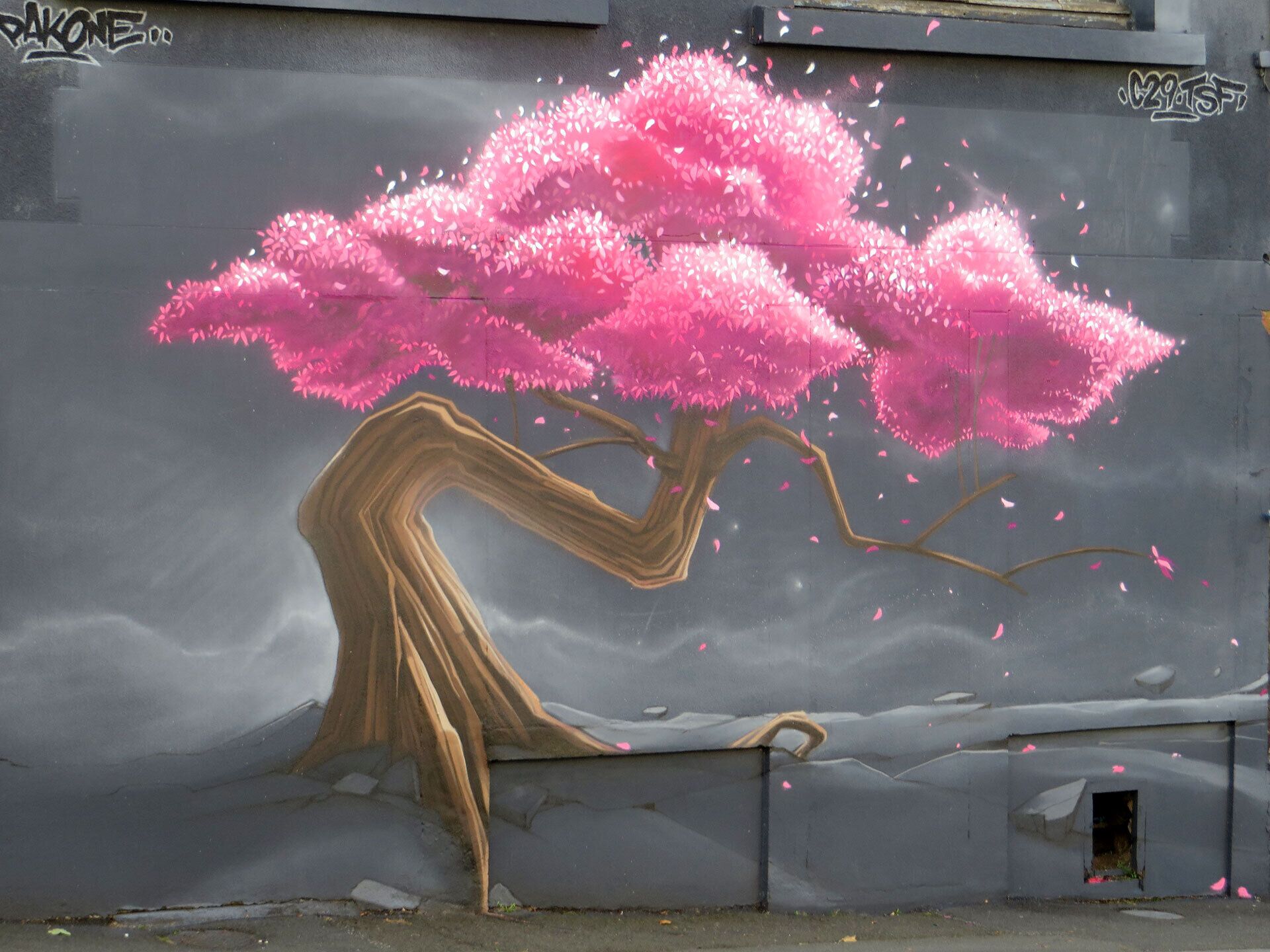 Ein Wandgemälde eines rosa Kirschblütenbaums an einer grauen Wand.