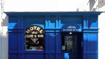 A blue building with a sign reading "HOTEL du CHAMP DE MARS".