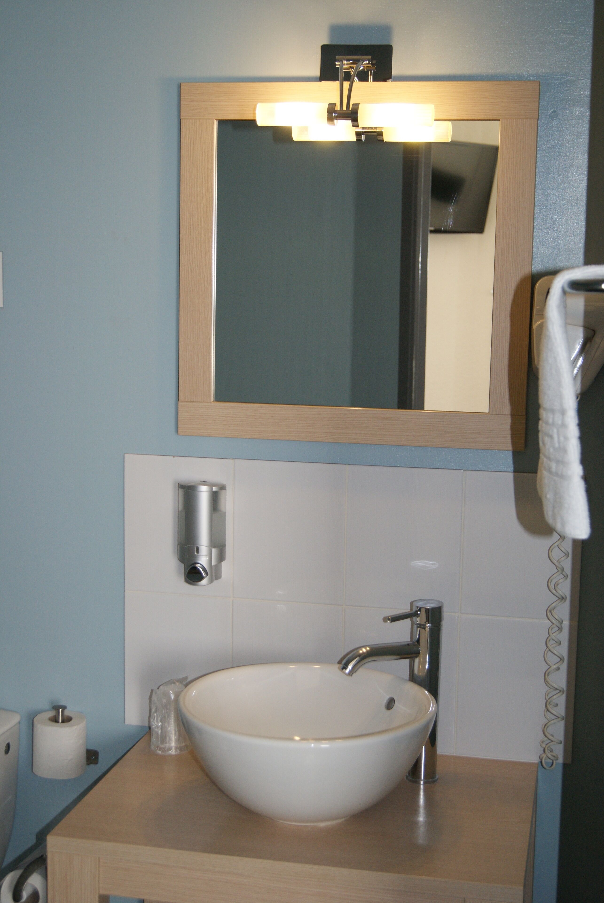 A bathroom with a white sink, a mirror, a towel hanging on the wall, and a soap dispenser.