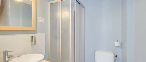 Un baño con lavamanos blanco, un espejo, un inodoro y una cabina de ducha de vidrio.