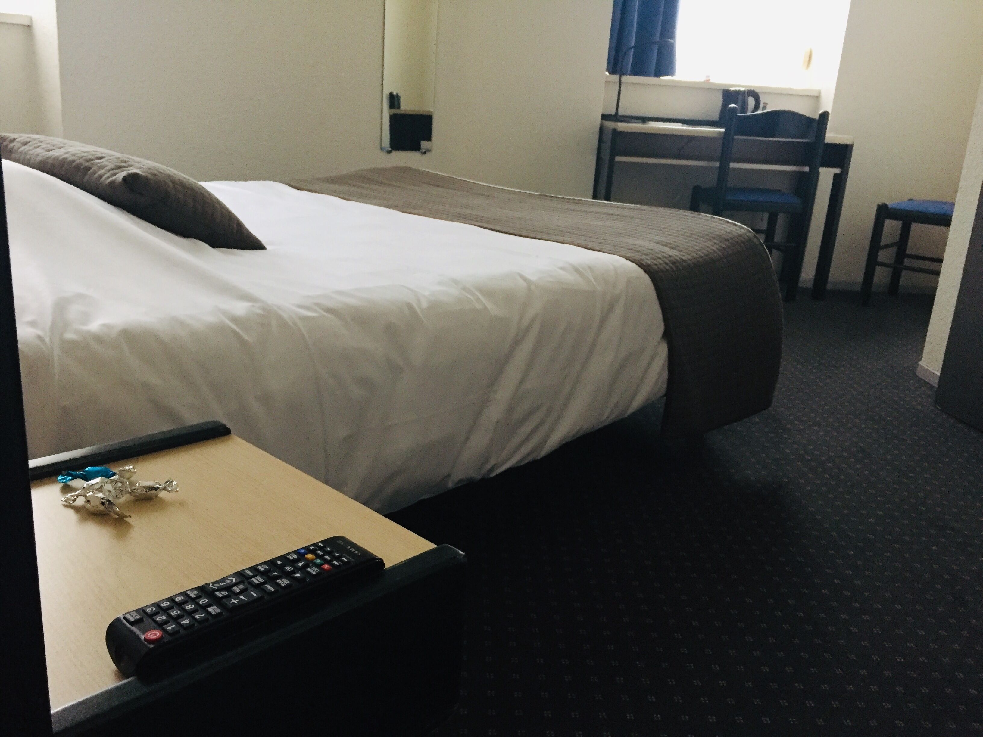 Quarto de hotel com cama, escrivaninha e cadeira.