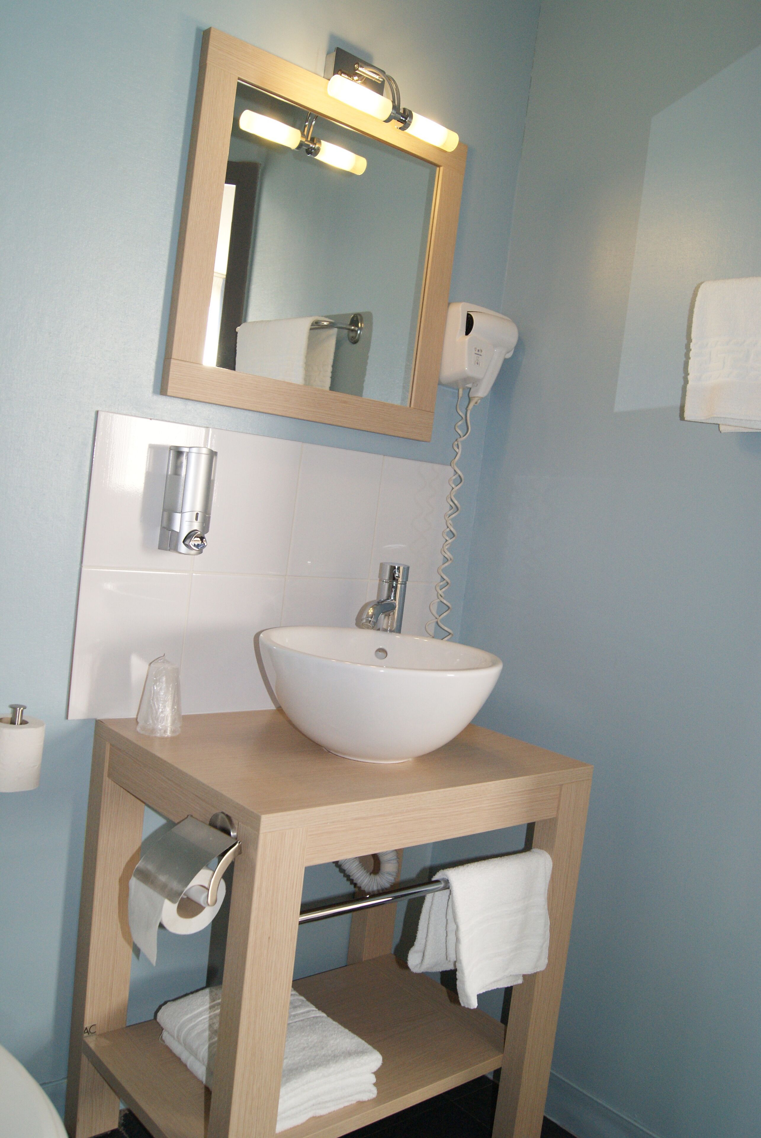 Une salle de bain avec un meuble-lavabo en bois, un lavabo blanc, un miroir, un porte-serviettes et un sèche-mains.