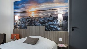 Quarto de hotel com um grande mural panorâmico, uma cama com travesseiro, uma mesinha de cabeceira, uma luminária e uma bolsa na parede.