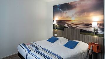 A hotel room with a bed, two lamps, a painting of a sunset, and a handbag on the nightstand.