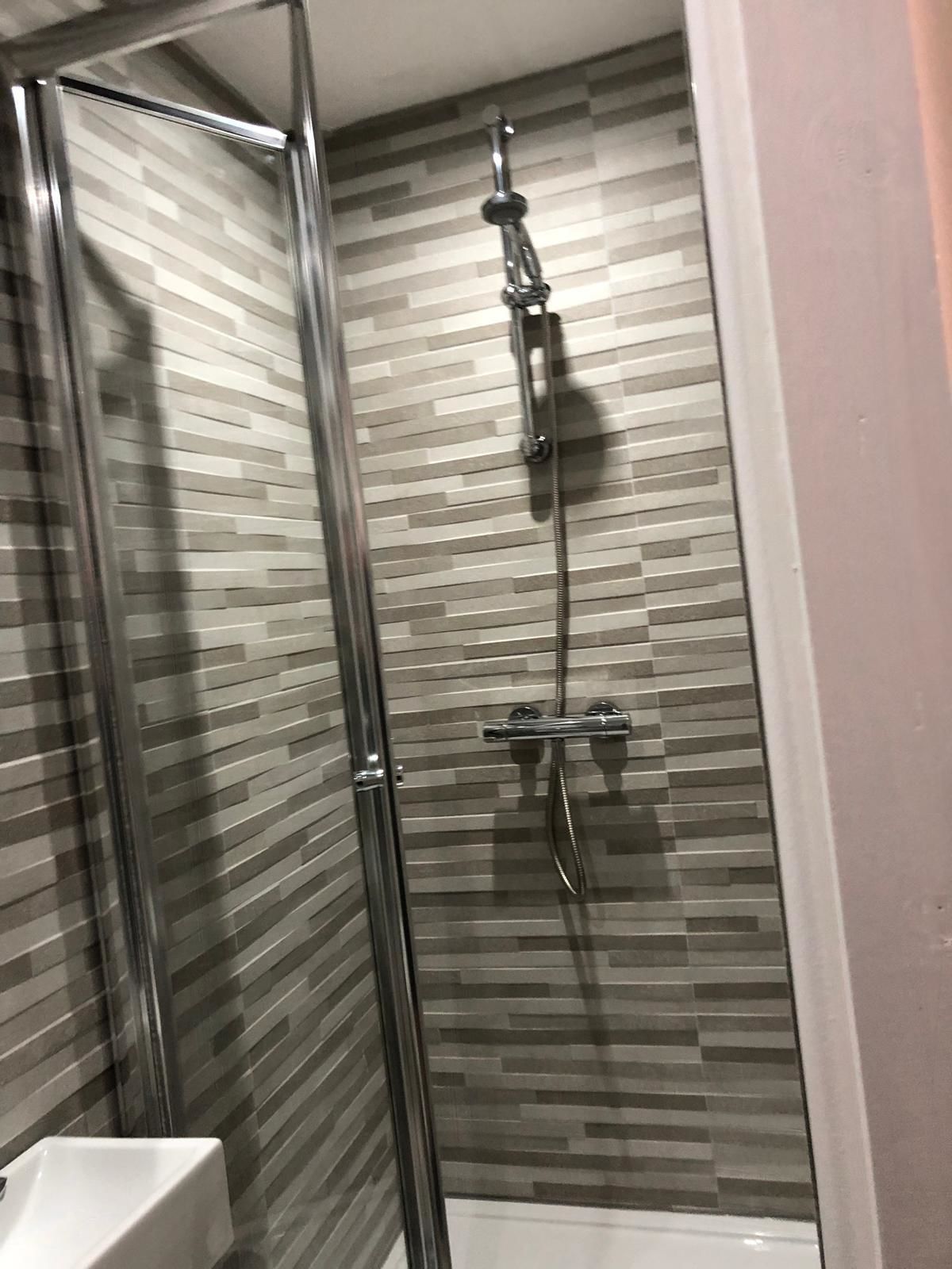 A glass-enclosed shower with a tiled wall and a white bathtub.