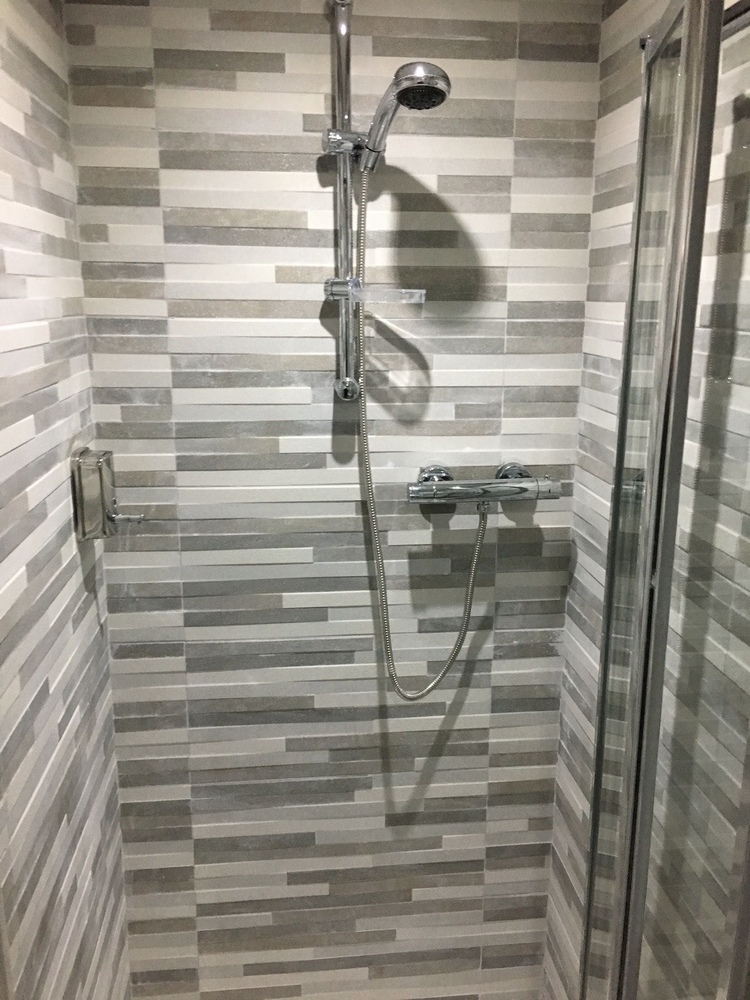 Chuveiro com porta de vidro, chuveiro manual e torneira fixada na parede.