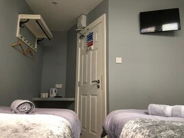 Un dormitorio con dos camas, un televisor montado en la pared, una puerta con letrero de seguridad contra incendios y un estante pequeño con una tetera.