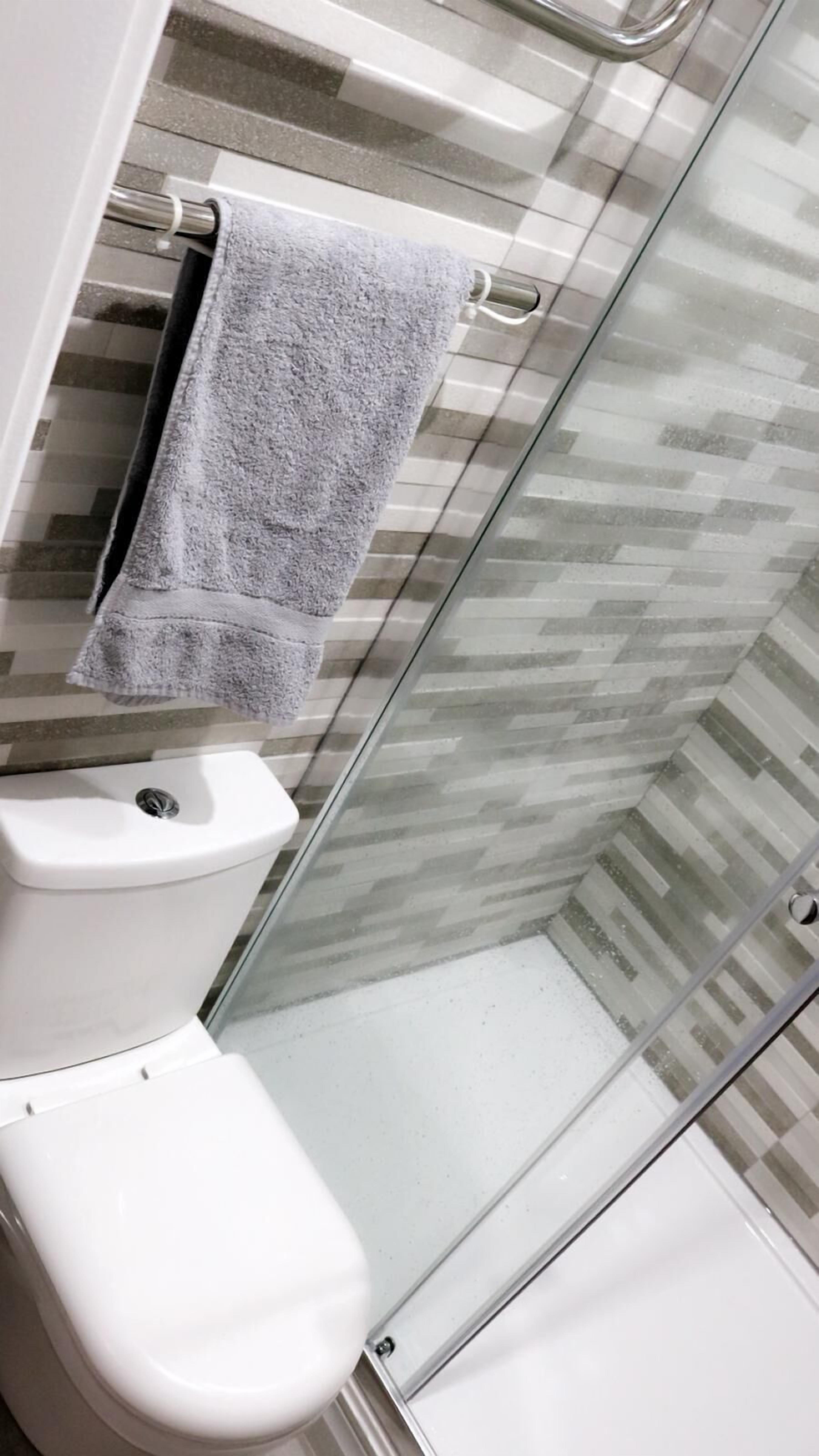 A bathroom with a white toilet, a glass shower enclosure, and a towel hanging on a metal rack.