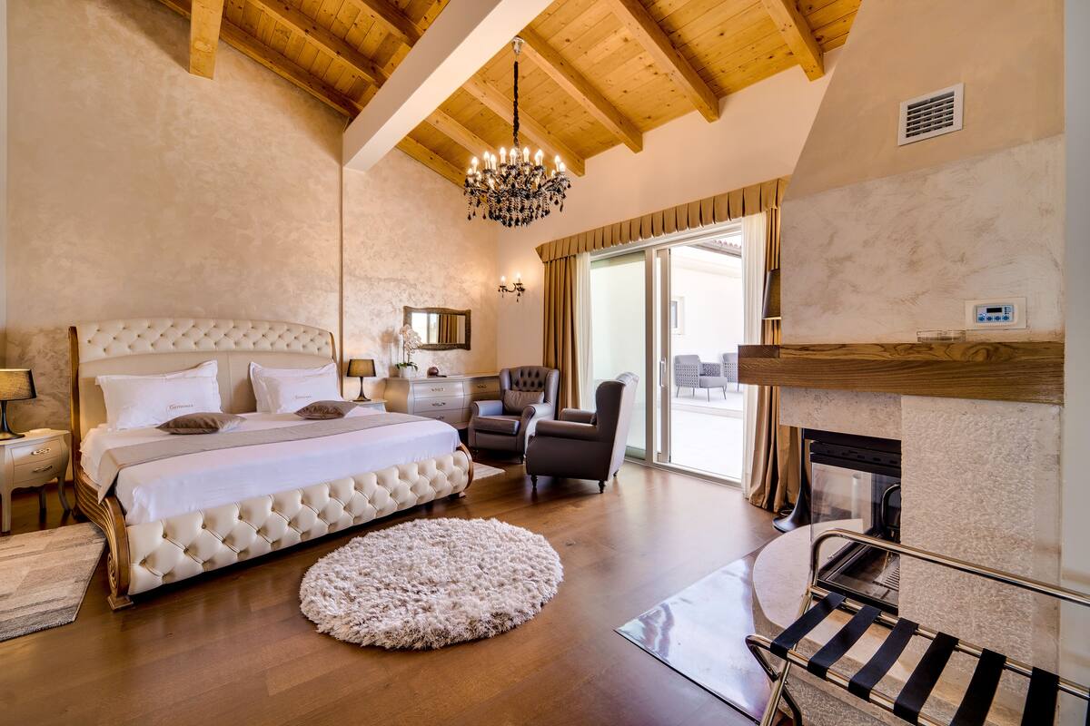 Een slaapkamer met een groot bed, een kroonluchter, een open haard en uitzicht op de omgeving.