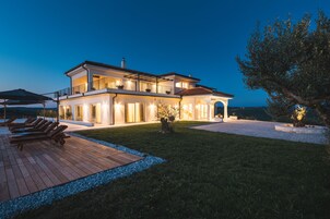Una casa de dos pisos con un patio, mobiliario exterior y una entrada bien iluminada.