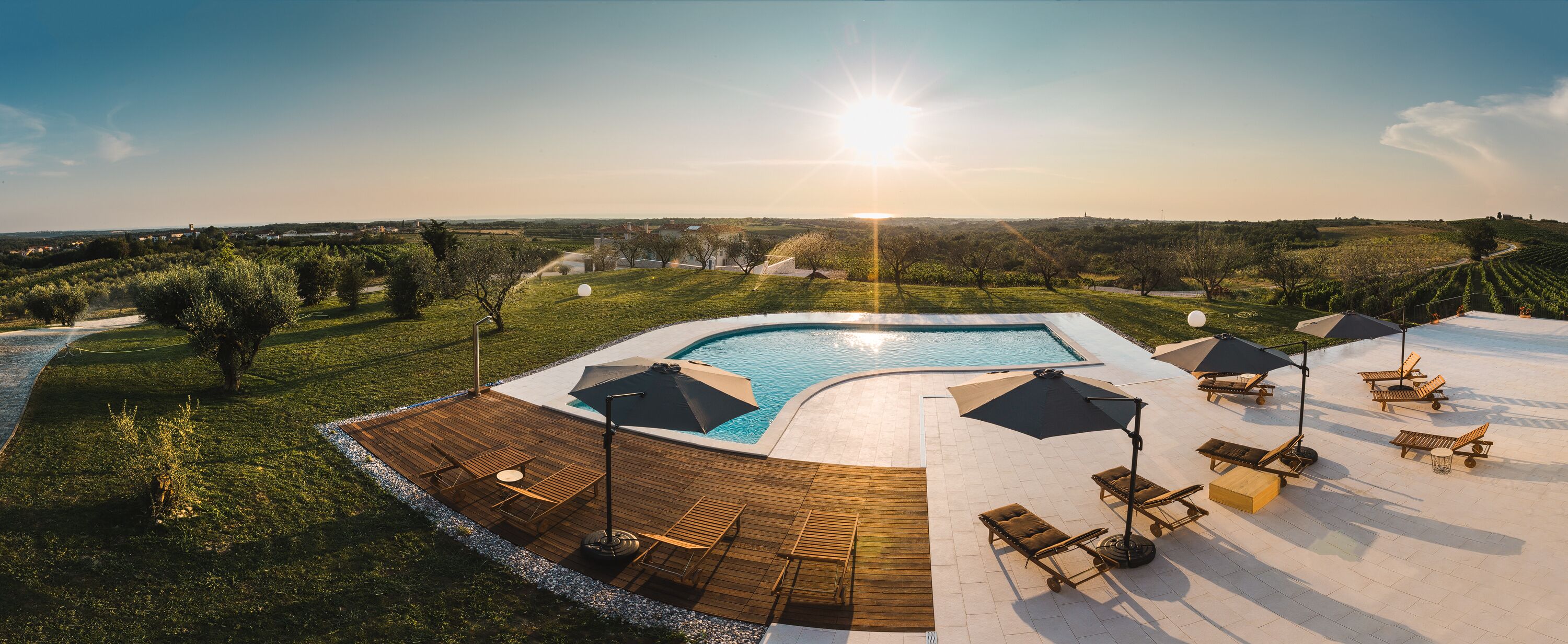 A pool area with a wooden deck, lounge chairs, and umbrellas.