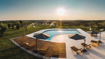 A pool area with a wooden deck, lounge chairs, and umbrellas.