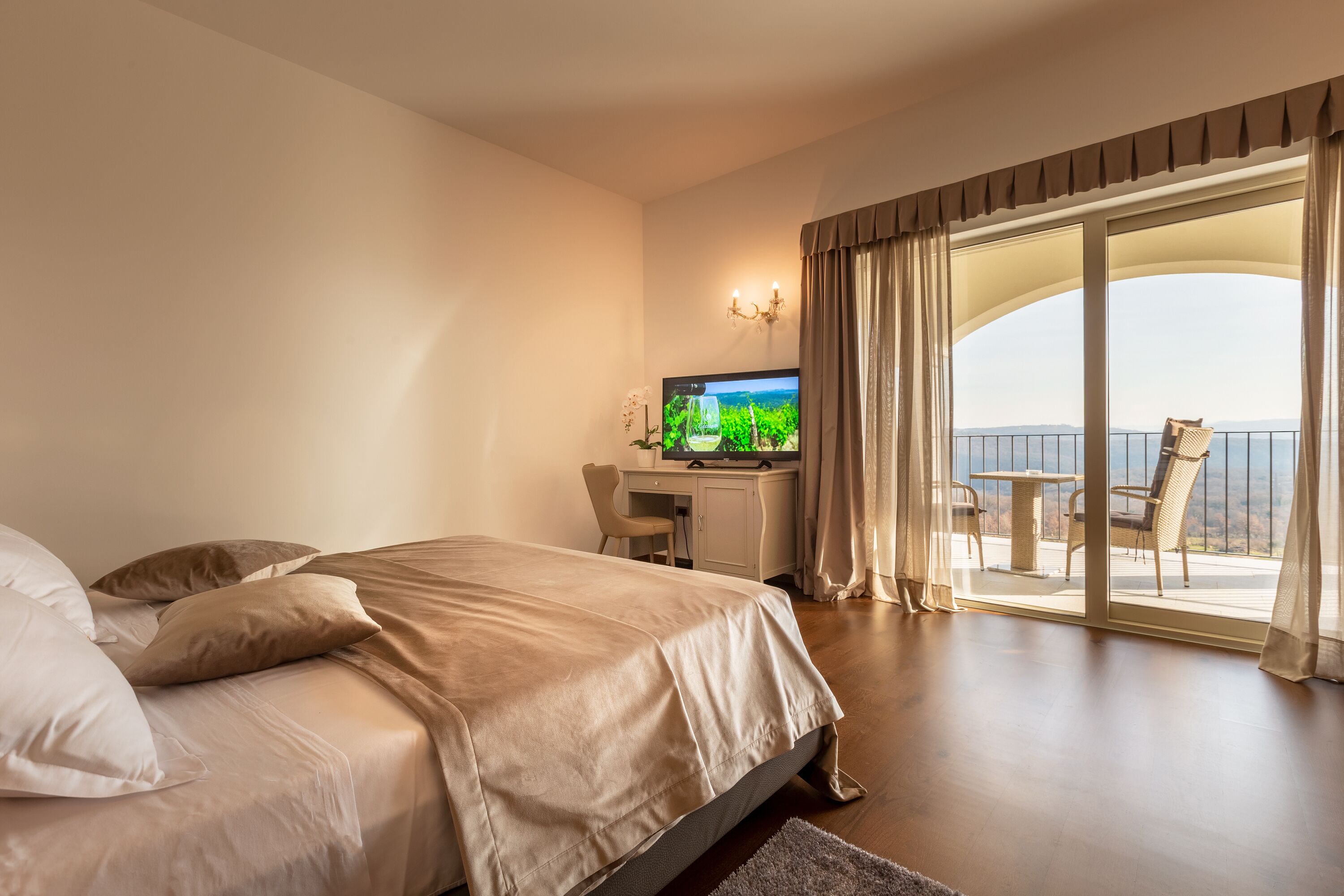 Quarto de hotel com cama, escrivaninha com computador e varanda com vista.