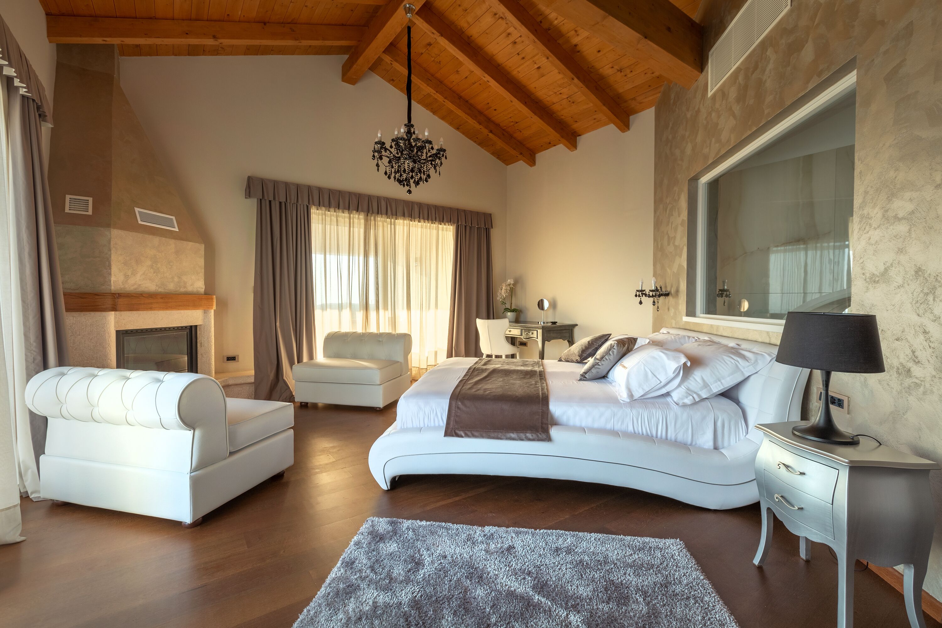 Une chambre moderne avec un grand lit, un canapé, une cheminée et une grande fenêtre.